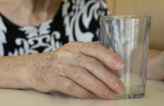 Mano de una anciana sosteniendo un vaso de cristal.