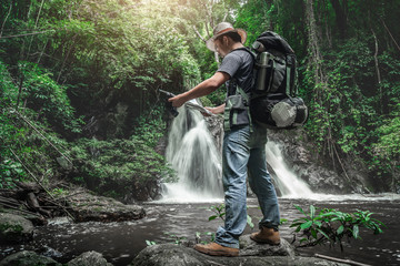 Traveler with backpack standing by waterfall and looks at map, holidays and tourism Concept