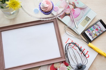 frame with a white sheet of paper lies on the table bleached oak, lying around objects: kitchen scales, yellow flower, whisk for whipping, phone