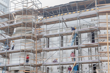 Professional construction workers on the scaffold elevator insulated wall facade with mineral wool. roofers wearing safety harness insulating wall facade at height on old building in a crane