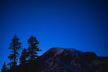 Night sky with trees in mountains being lit by the moon