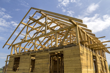 New cottage of natural ecological lumber materials under construction in green field. Wooden walls and steep roof frame. Property, investment, professional building and reconstruction concept.