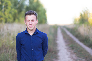 portrait of a guy in a blue shirt against a background of trees and a dirt road to the field