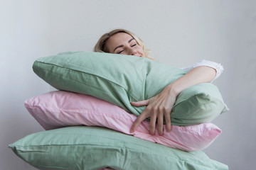 Beautiful blonde girl holds a lot of pillows in her hands. She lies on them with pleasure