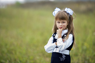 Close-up portrait of cute adorable confident first grader girl in school uniform and white bows in...