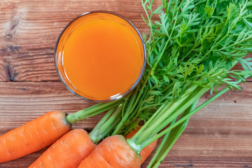 Fresh carrot juice in glass and carrots on a wooden table