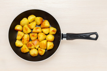 Frying pan with fried potatoes on a light wooden surface