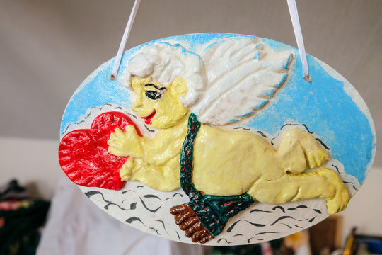 Cupid with a red heart in his hands. Handmade pendant decoration from dough.