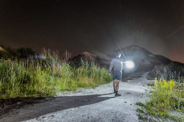 Man with a bright glowing lantern in his hand goes at night in the mountains along the path