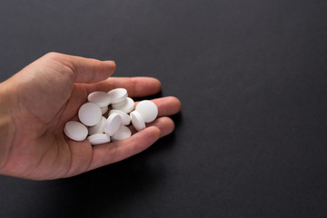 Close up white pills in hand isolated on black background. Medicine, narcomania, treatment.