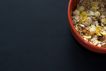 Close up muesli in ceramic red bowl isolated on black background. Heathy food, breakfast.