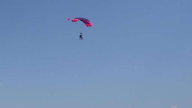Red and blue parachute descends down against the blue sky
