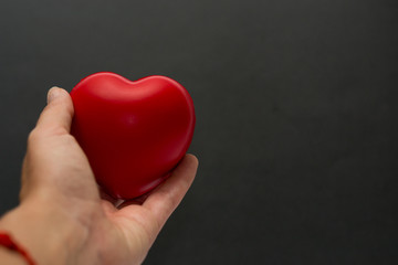 Fototapeta premium Close up red heart symbol of love isolated on black backgroound. Hand holds red heart. St. Valentines day. Objecr photography. Health and cardiovascular risk of diseases. Cardiology news. 