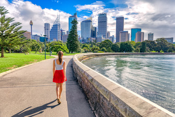 Sydney city girl tourist walking in urban park with skyscrapers skyline in the background. Australia travel vacation in the summer. Australian people lifestyle living.