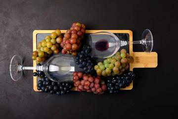 Two wineglasses with red and white wine and grapes on dark wooden background. Top view. Flat lay. Copy space