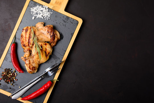 Grilled chicken fillets on slate plate with rosemary, pepper and spices on dark wooden background. Top view. Flat lay. Copy space