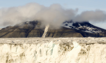 Edge of a Glacier with Ice Pack and Foggy, Cloudy, Snow Capped Mountains in the Background, on the Edge of the Arctic Ocean on the Coast of Spitsbergen Svalbard Archipelago in Northern Norway