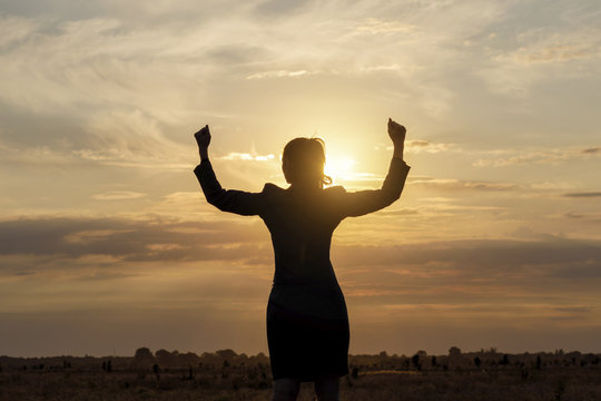 Businesswoman with arms raised against the sun.