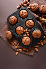 Homemade chocolate muffins (brownies) with cinnamon, almonds and hazelnuts on brown paper background