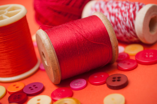 closeup of buttons and bobbins of cotton yarn on red background