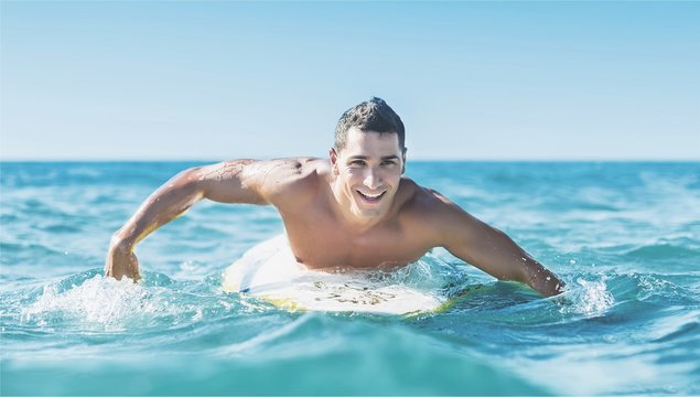 Handsome young surfer floating in blue water