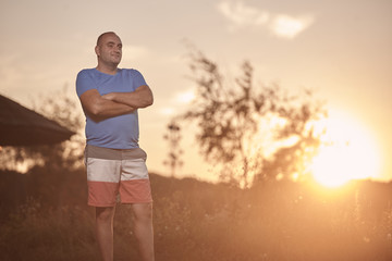 Fototapeta na wymiar one young overweight man, 30-35 years, proud, posing standing, golden orange sunset, sun, outdoors nature landscape, rural area.