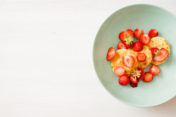 Homemade curd pancakes with strawberries in a beautiful fashionable mint-colored dish on a light wooden background