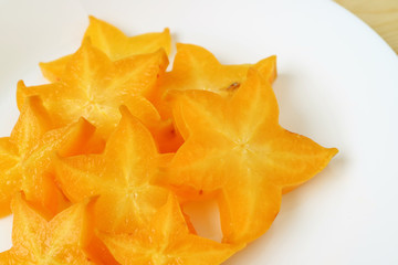 Fototapeta premium Top view of vivid orange yellow color fresh ripe Star Fruit sliced in many pieces served on white plate 