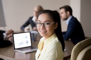 Head shot portrait of smiling asian female sitting at the desk in office looking camera at...