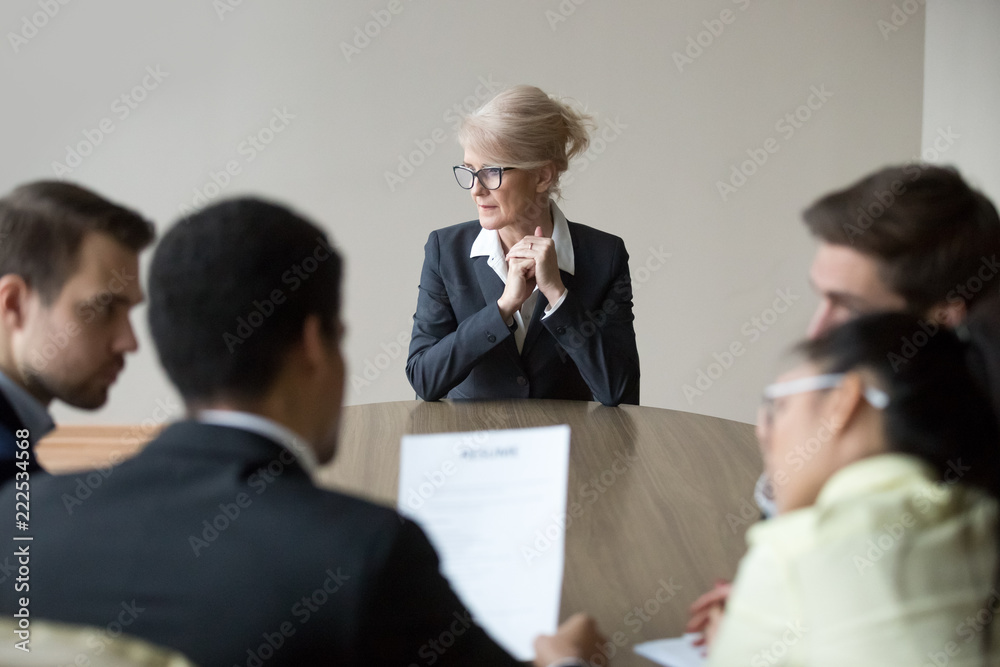 Sticker middle aged stressed woman sitting at the desk in office at meeting. young multiracial workers team 