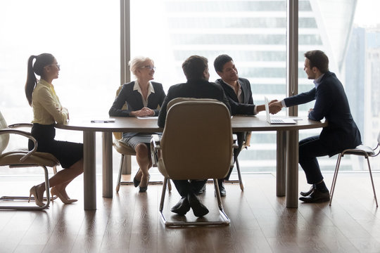 Smiling multiracial business people sitting at meeting in conference room and handshake. Asian, african, american professional workers. Good work results, reach agreement and signing contract concept
