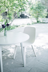White table with flowers and a white chair in a green yard in a summer sunny day