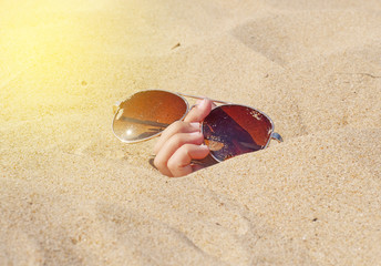 Fototapeta na wymiar Human hand holding sunglasses out of the hole on the sandy beach