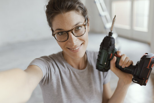 Cheerful woman holding a drill and taking a selfie