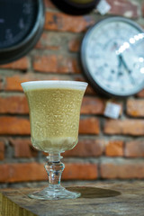 Cappuchino coffee in glass goblet on the wooden table and clocks on the brick wall