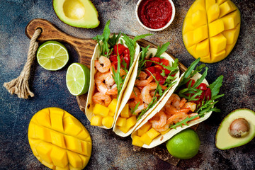 Mexican shrimp tacos with avocado, tomato, mango salsa on rustic stone table. Recipe for Cinco de...