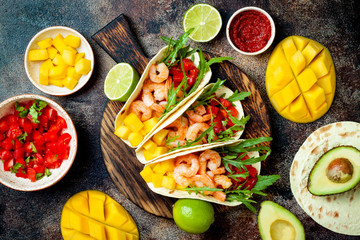 Mexican shrimp tacos with avocado, tomato, mango salsa on rustic stone table. Recipe for Cinco de...