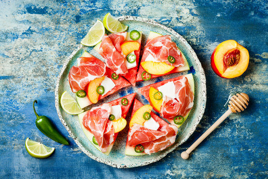Fresh Summer Watermelon Pizza With Feta Cheese, Peach, Prosciutto, Jalapeno And Honey Drizzle On Blue Background