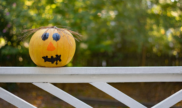 A great halloween background photo of a pumpkin with a face painted on it setting on a railing.