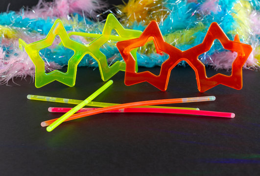 Neon Party supplies and Colorful Feather Boas on black background - colored led party lights - Photo booth Props. Copy Space. Party background