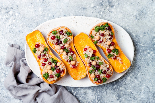 Stuffed butternut squash with chickpeas, cranberries, quinoa cooked in nutmeg, cloves, cinnamon. Thanksgiving dinner recipe. Vegan healthy seasonal fall or autumn food