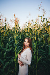 Young beautiful woman stands in a dress among ripe corn. Agroculture.
