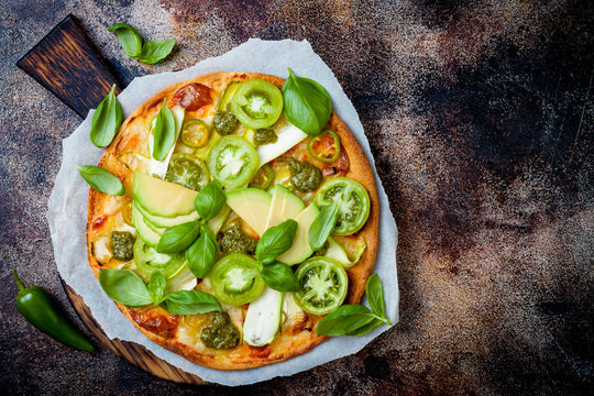 Green pizza with pesto, zucchini, tomatoes, avocado, jalapeno, mozzarella cheese and fresh basil