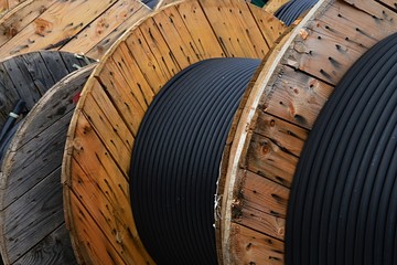 Detail of thick isolated electric cables coiled on wooden cable reels in storage
