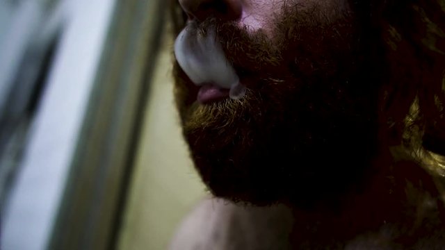 Long Red Hair bearded man smoking in dirty outdoor area of a complex