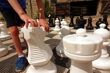 The hands and feet of a boy moving the knight piece on a giant outdoor chess board