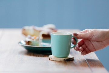 Female hand holding cup near pate with eaten cake and spoon on wooden table. Side view