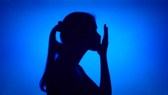 Silhouette of young frustrated woman. Female's face in profile in despair on blue background. Black contour shadow of sad teenager's half-face showing strong negative emotions