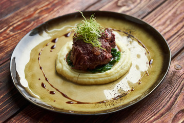Braised beef with red wine, close-up. Jerusalem Artichoke Puree, spinach and truffle oil with baked meat in aceramic plate at restaurant table