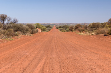 A dead straight, red, gravel road leading to the flat horizon of the Northern Territory outback, Australia.